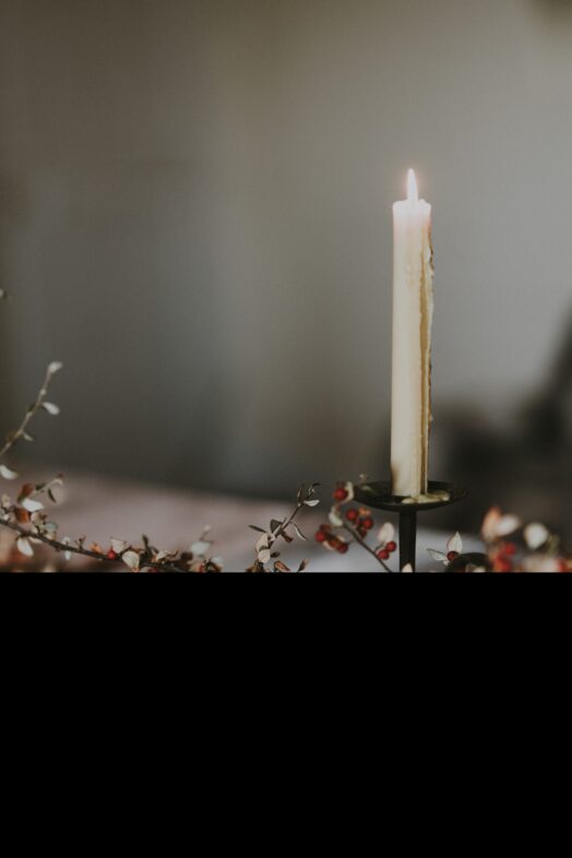 En tänd ljus på en ljusstake omgiven av torkade blommor på ett bord.